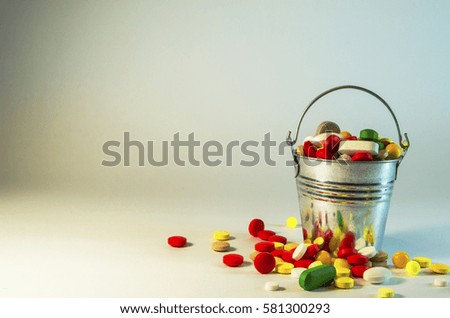 multicolored pills are in a metal bucket standing on a white background
