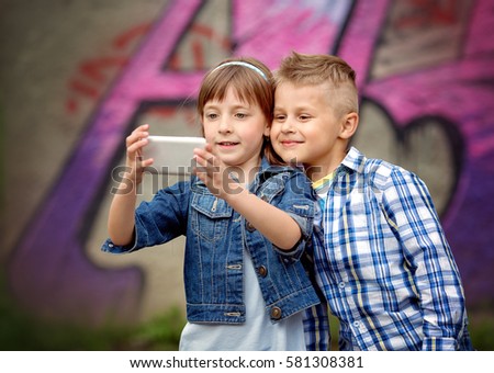 Portrait of happy fashion little kids taking selfie by painted wall