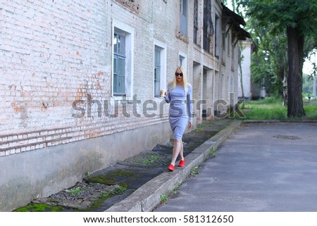 Woman blond hair slim athletic figure near brick wall stands wearing sunglasses.