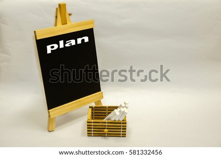 Small blackboard written "plan" and white chalks inside wooden box on the white table