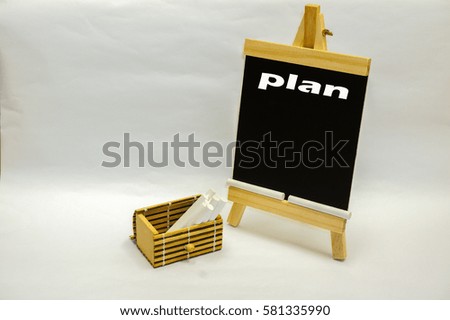 Small blackboard written "plan" and white chalks inside wooden box on the white table