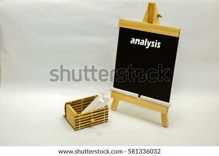 Small blackboard written "analysis" and white chalks inside wooden box on the white table