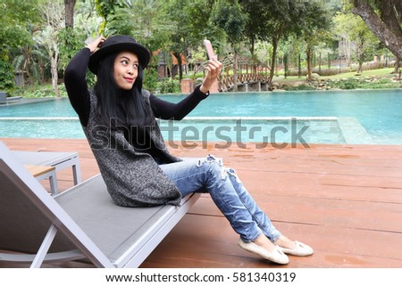 Charming beautiful tan skin Asian woman hand use phone and laptop side swimming pool . Presenting your product with good looking chic business woman.