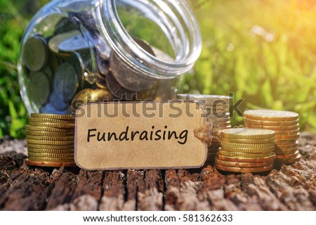 Business Concept - Paper tag written with FUNDRAISING inscription. Coins stack, jar and nature background.  Royalty-Free Stock Photo #581362633