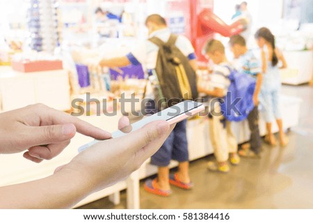 Man using mobile phone, blur image of children in toy store as background.