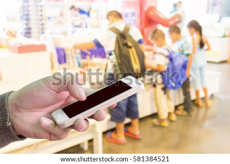 Man using mobile phone, blur image of children in toy store as background.