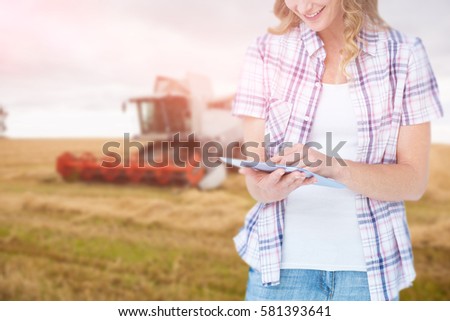 Pretty hipster using tablet against combine harvester machine working on field