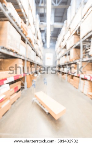 Blurred large furniture warehouse with flatbed cart forklift. Row aisles, bins, shelves from floor to ceiling. Defocused industrial storehouse interior. Inventory, wholesale, logistic, export concept.