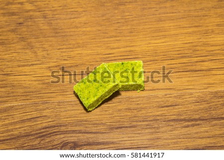 Dehydrated bouillon stock cube salty meat and vegetables aromatic yellow spice, ingredient single whole condiment portion wrapped, open in paper pack on wooden background