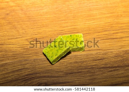 Dehydrated bouillon stock cube salty meat and vegetables aromatic yellow spice, ingredient single whole condiment portion wrapped, open in paper pack on wooden background