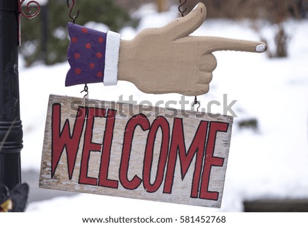 A welcome sign hang below a hand pointing the direction.