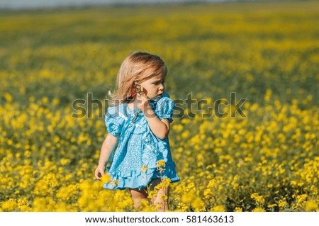Portrait of a little girl in a blue dress in field with yellow flowers