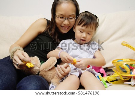 Mother and daughter on sofa, playing with toys