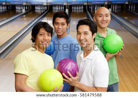 Four men in bowling alley, holding bowling balls