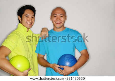 Two men holding bowling balls, smiling at camera