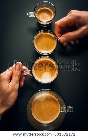 Cups of coffee in ascending order on the black background. man's and woman's hands holding a cups. Royalty-Free Stock Photo #581592172