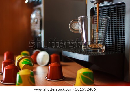 A cup of fragrant coffee on the coffee machine. Coffee pouring into the cup. Wooden table background. Royalty-Free Stock Photo #581592406