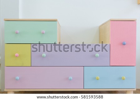 A shelf have many colorful drawer place close to the wall.
