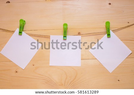 A rope with clothespins green holding a white paper on the wooden background