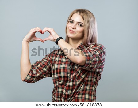 Portrait of attractive young woman with heart shaped hands on grey background