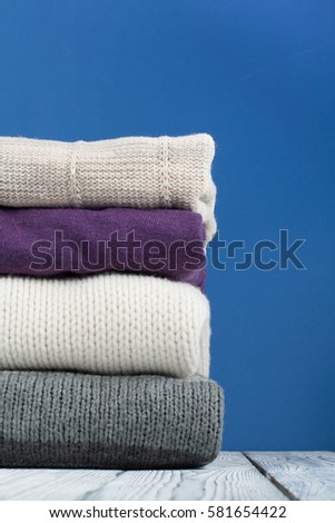 Knitted wool sweaters. Pile of knitted winter, autumn clothes on blue, wooden background, sweaters, knitwear, space for text.