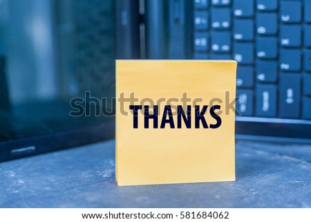 THANKS word on blank note on wooden table over blurry laptop as a background