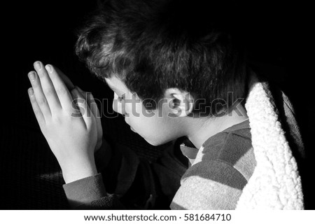 Young boy kneeling to pray at bedtime, eyes closed, picture of innocent Christian faith, religious concept