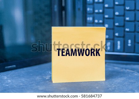 TEAMWORK word on blank note on wooden table over blurry laptop as a background