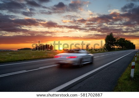Speeding motion blur white car on the road in a rural landscape at sunset. Royalty-Free Stock Photo #581702887