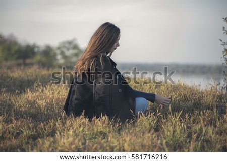 Thoughtful sad, melancholic girl sitting in the grass, running through her memories Royalty-Free Stock Photo #581716216