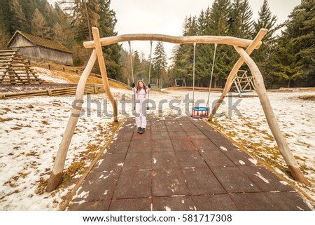 Happy woman rocking on the swing in a snowy park in mountains