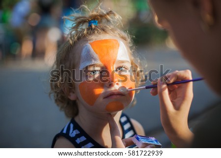 boy face close-up with red colors on his face, facepainting watercolor, artist paints watercolor paints tiger mask, draw on the boy's face paints picture, orange ink for drawing the tiger