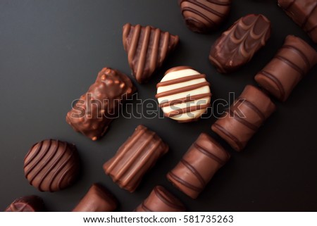 Line of chocolates of different shapes on a black background. all the candy black and milk chocolate, one white round candy. Royalty-Free Stock Photo #581735263