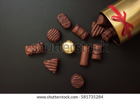 Chocolates in different shapes and colors spilled from the gold round box with a red bow on a black background. among all the sweets have a gold-wrapped in the color of the box Royalty-Free Stock Photo #581735284