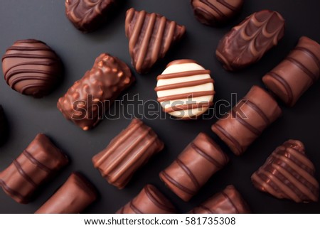 Line of chocolates of different shapes on a black background. all the candy black and milk chocolate, one white round candy. Royalty-Free Stock Photo #581735308