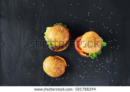 Craft beef burgers with vegetables. Flat lay on black textured background with sesame seeds.