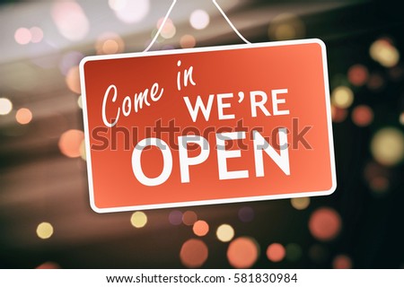 We are open sign hanging on a glass storefront