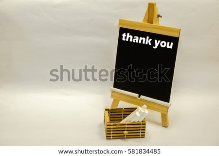 Small blackboard written "thank you" and white chalks inside wooden box on the white table