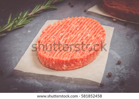 Raw burgers on parchment paper with rosemary. Grey marble background