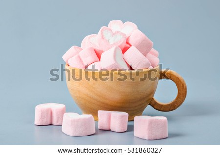 Heart shape pink marshmallows in wooden cup on gray background.