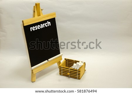 Word "research" written down on mini blackboard and chalks inside wooden container isolated over white background