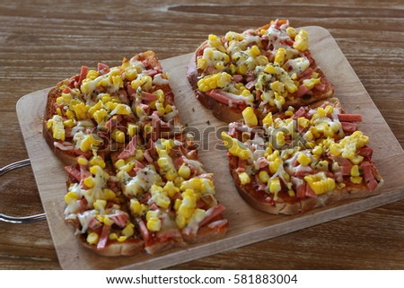 left over of Homemade mini pizza from toast with ham,yellow corn and cheese serving on  wood cutting board, on a wooden table close up.Don't want to wast the food
