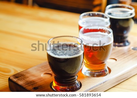 Flight with various types of craft beer in small glasses on a wooden table in a pub Royalty-Free Stock Photo #581893654
