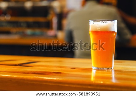 Nonic pint glass with pale ale standing on a wooden table in a pub Royalty-Free Stock Photo #581893951