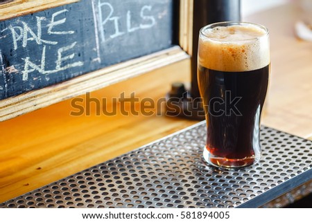 Nonic pint glass with dark stout ale standing on a pub counter near draft taps Royalty-Free Stock Photo #581894005