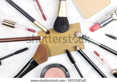 Makeup brushes, pencils, lipstick et al on a light background, with a blank kraft business card for copy space. A horizontal template for a makeup artist's business card or flyer design