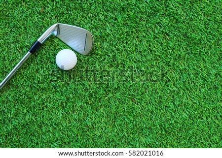 Golf ball and golf club on green grass.