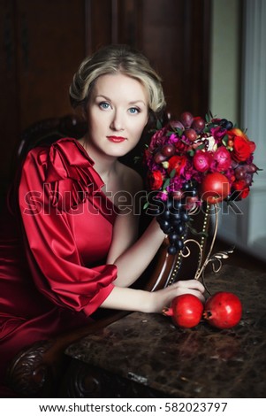 beautiful young woman in a red dress with red flower arrangement. composition of flowers and fruits of pomegranate and grape