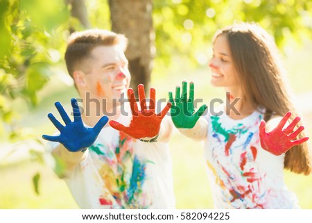 Pretty boy and girl showing their painted hands to the camera and smiling. In front of camera in focus there are multicolored hands of pretty in love couple.