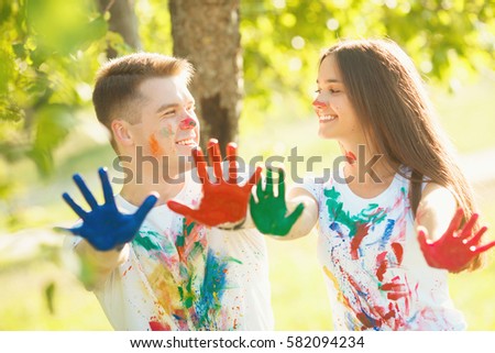 Pretty boy and girl showing their painted flat of the hands or palms at camera and smiling. In front of camera there are multicolored hands of pretty in love couple.